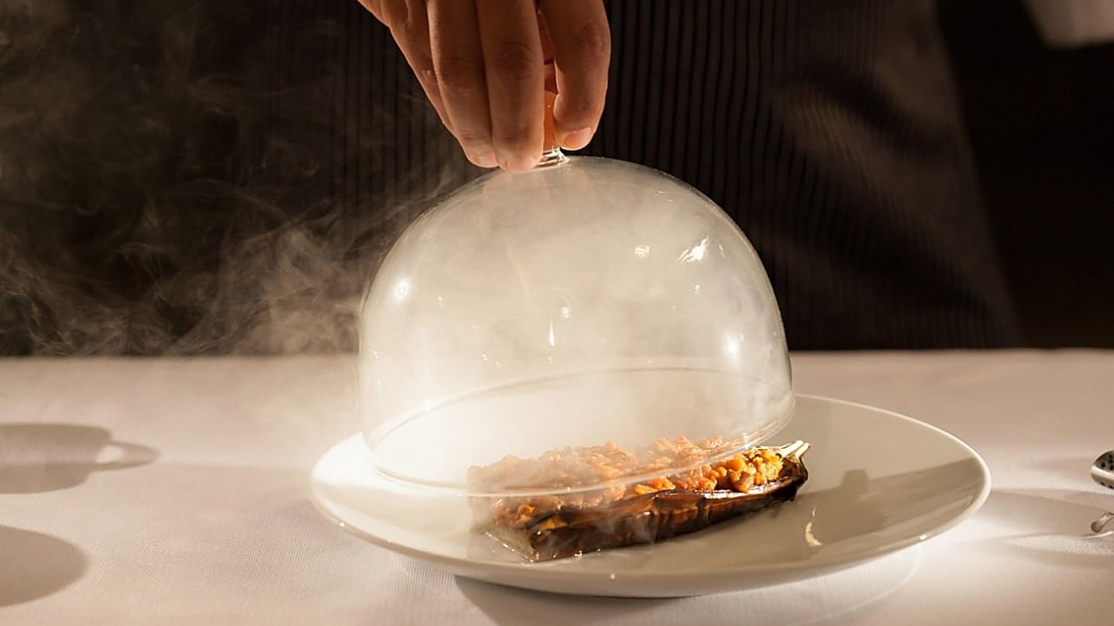 Glass cloche lifted, revealing a smoked dish